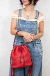 Person wearing overalls holding red Prada bag on white background