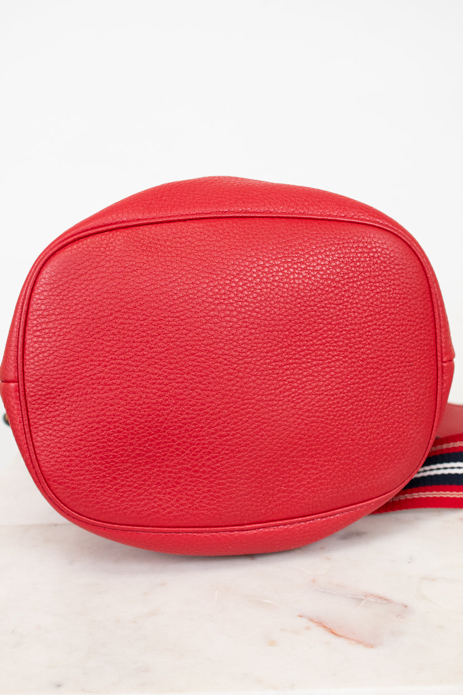 Red textured crossbody bag with a striped strap on a light background