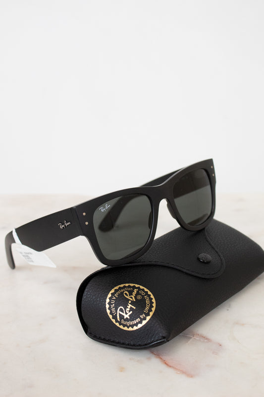 Black sunglasses with white accents on a black case with a gold logo, on a light marble surface.