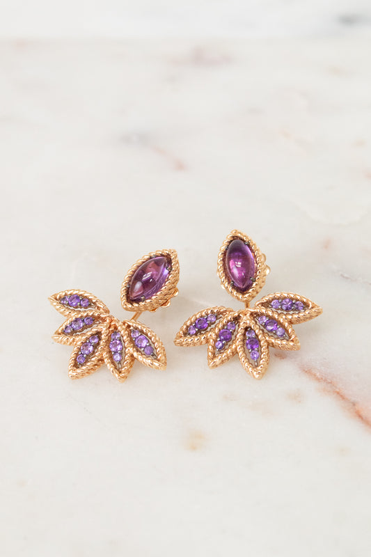 Gold earrings with purple gemstones on a marble surface
