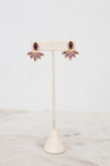 Purple and gold earrings on earring stand with white background