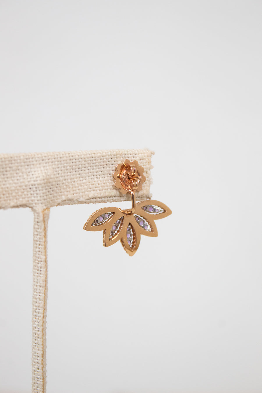 Gold leaf-shaped earring on a beige ribbon against a light gray background