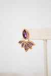 Gold earring with purple gemstones on a white background