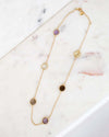 Gold necklace with various colored stones on a marble surface