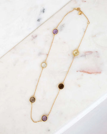 Gold necklace with various colored stones on a marble surface