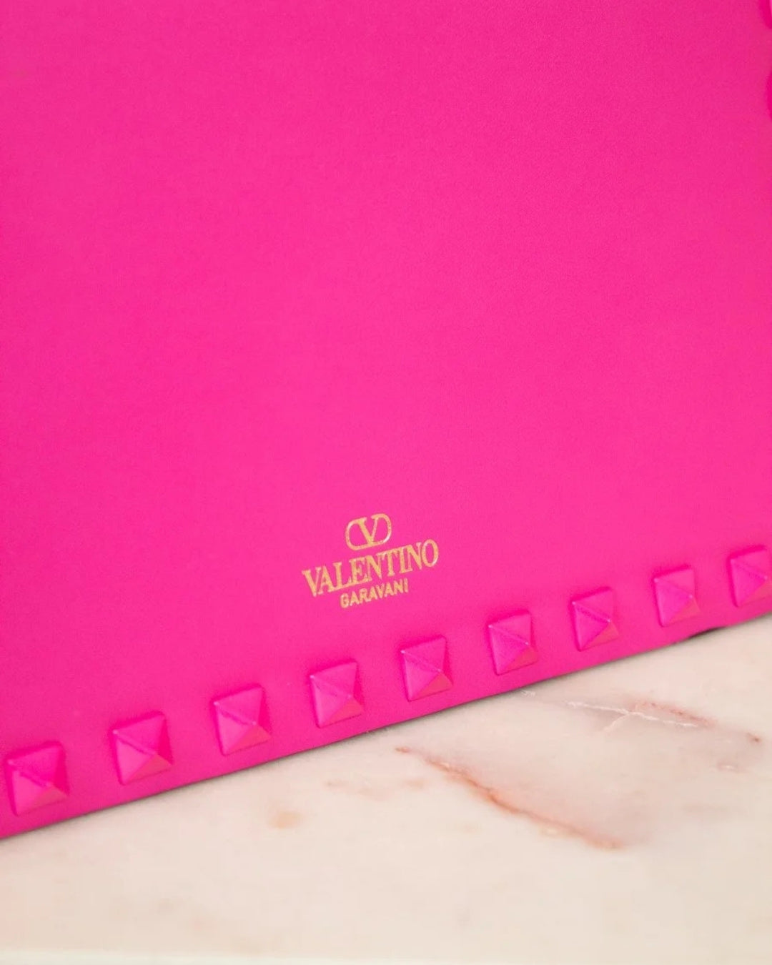 Pink clutch with studded details and Valentino logo on a marble surface