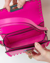 Pink handbag with gold studs held by a person's hands on a light background
