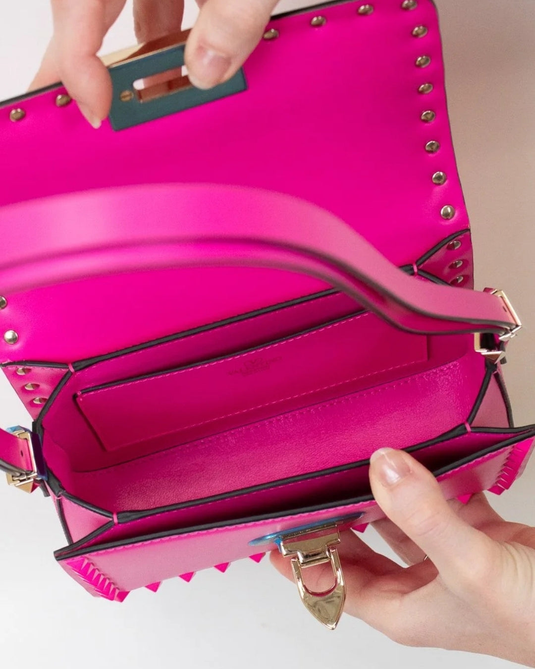 Pink handbag with gold studs held by a person's hands on a light background