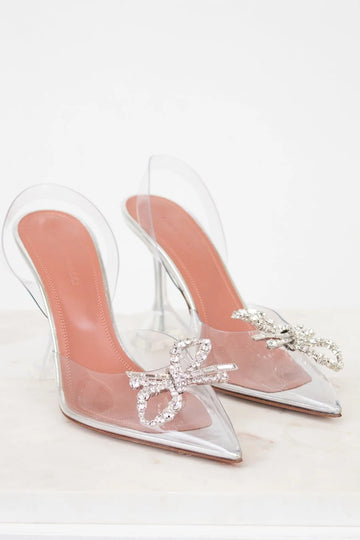 Clear high-heeled shoes with pink soles and decorative bows on a white background