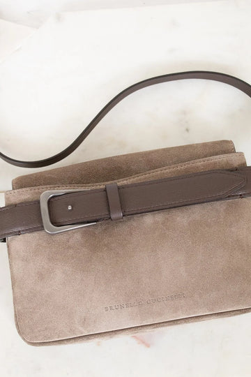 Beige suede handbag with a brown leather strap on a light background