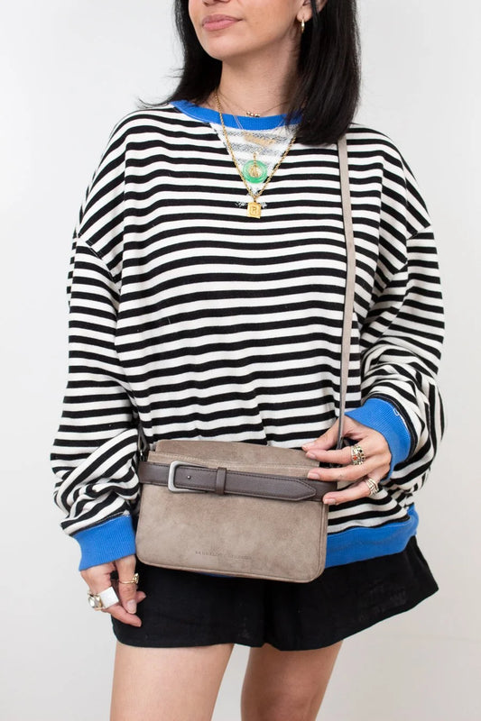 Person wearing a black and white striped sweater with blue accents, holding a beige handbag.