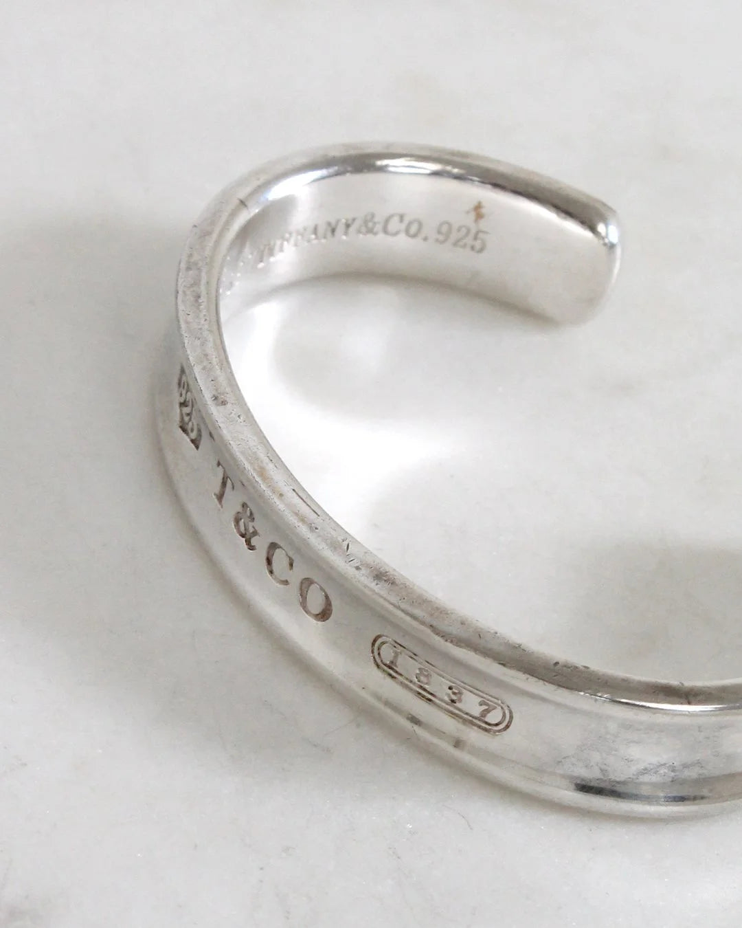 Silver ring with Tiffany & Co. engraving on a white marble surface