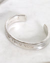 Silver bracelet with engraved text on a white marble surface