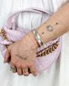 Hand with tattoos holding a pink quilted handbag with gold chain strap and wearing a silver cuff