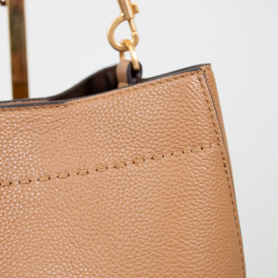 Close-up of a beige handbag with a gold handle on a light gray background