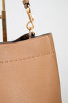 Close-up of a beige handbag with a gold handle on a light gray background