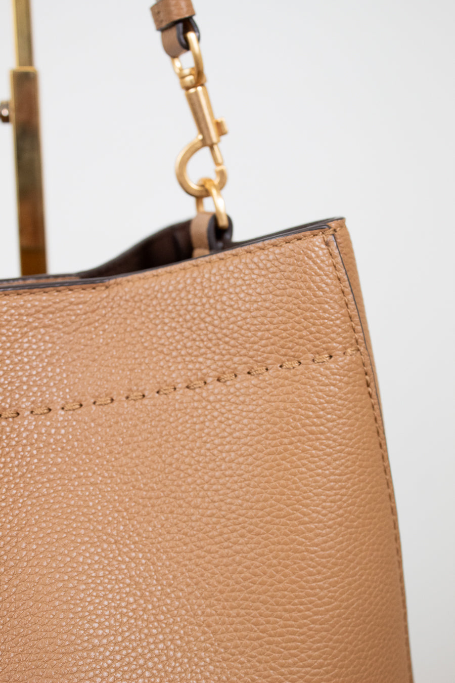 Close-up of a beige handbag with a gold handle on a light gray background