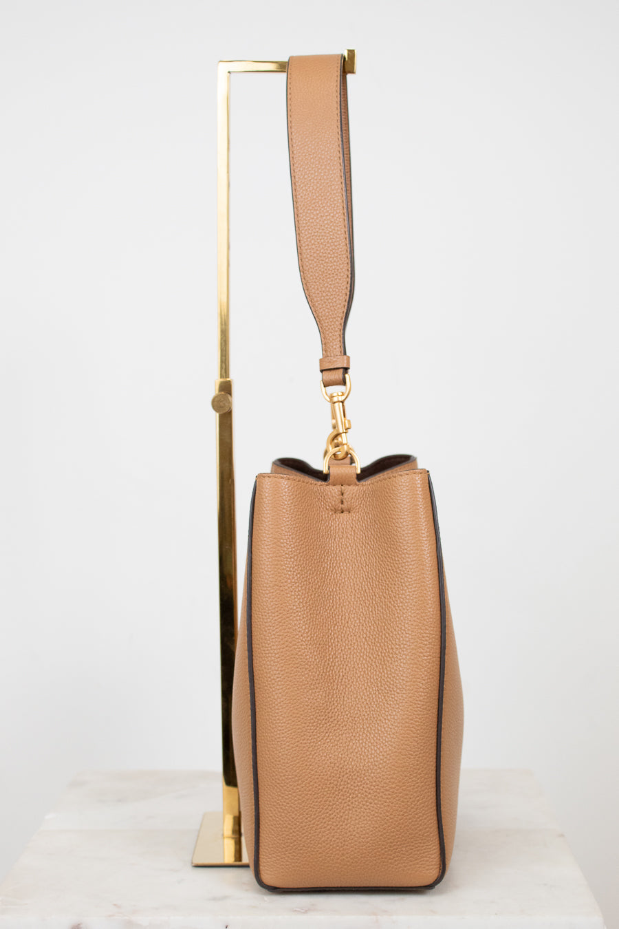 Tan handbag with a gold handle on a white background