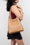 Person holding a tan handbag with a visible brand logo against a plain background