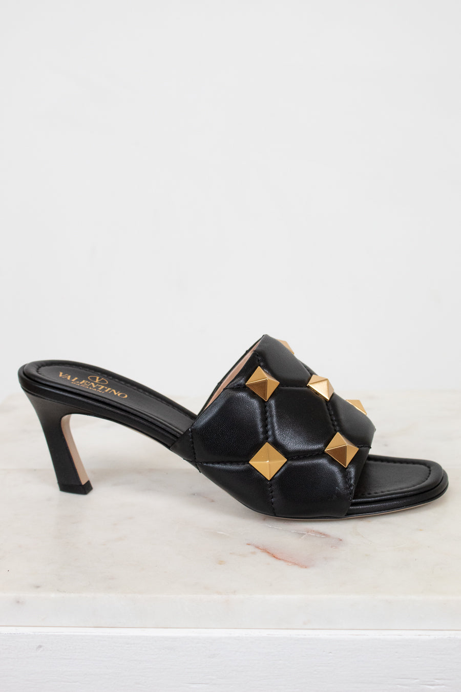 Side view of black leather heels with gold studs on white background