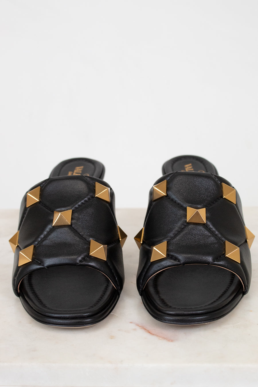 Black slides with gold pyramid studs on a light background