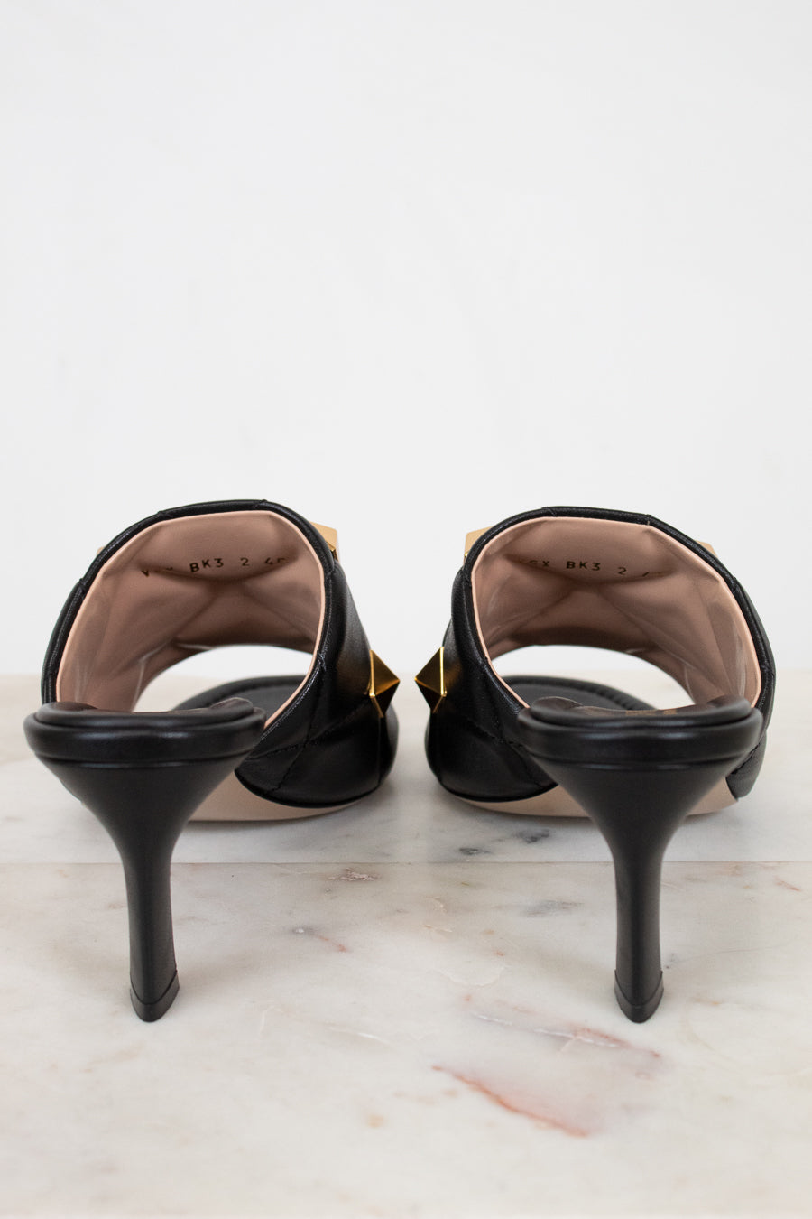 Black high-heeled shoes on a marble surface with a white background