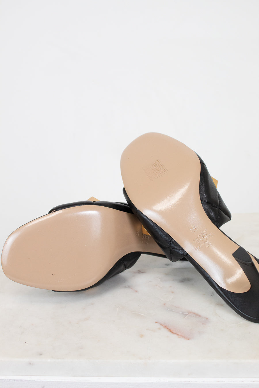 Pair of black high-heeled shoes with beige soles on a light marble surface.
