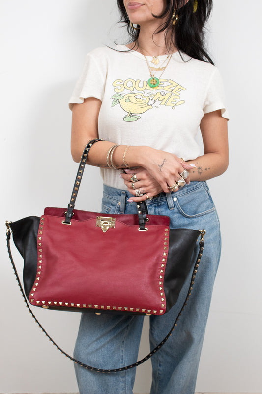 Person holding a red and black handbag against a plain background