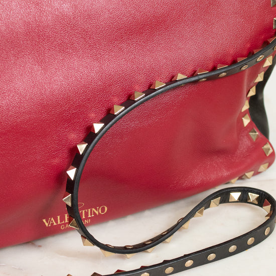 Red leather handbag with gold studs and a black strap on a light background