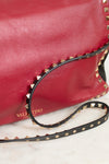 Red leather handbag with gold studs and a black strap on a light background