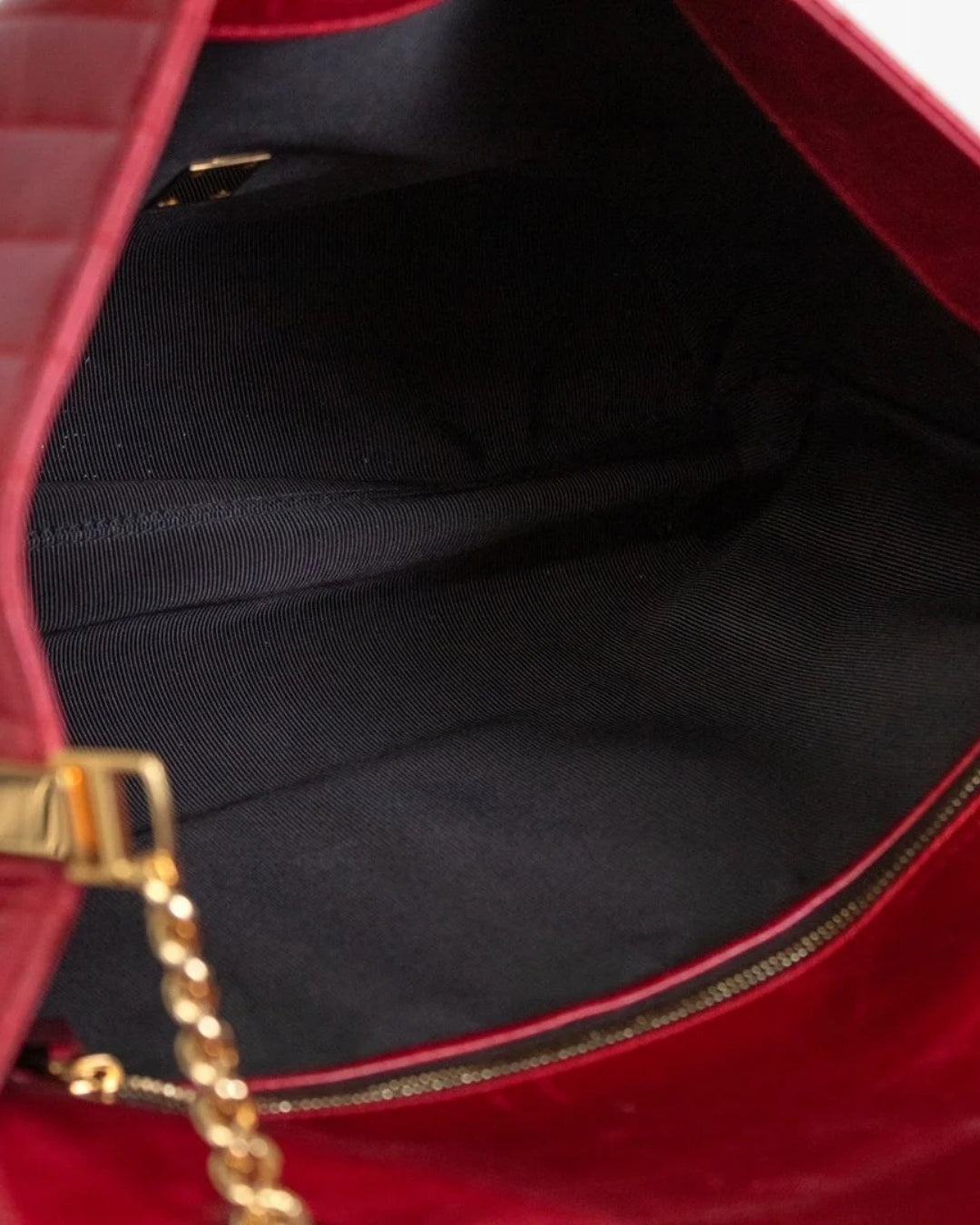 Close-up of a red handbag with gold chain detail on a black interior.