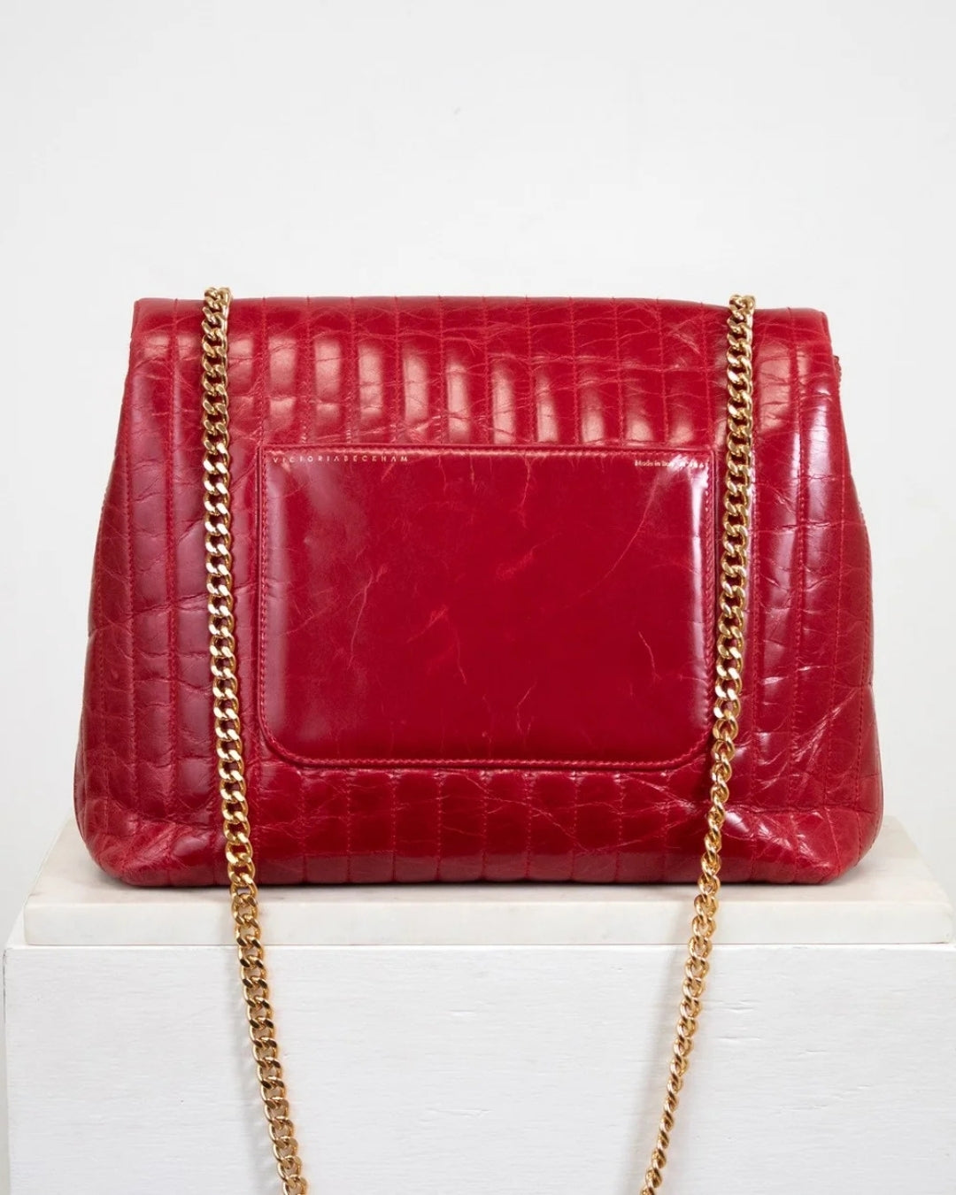 Red crocodile-patterned handbag with a gold chain on a white background