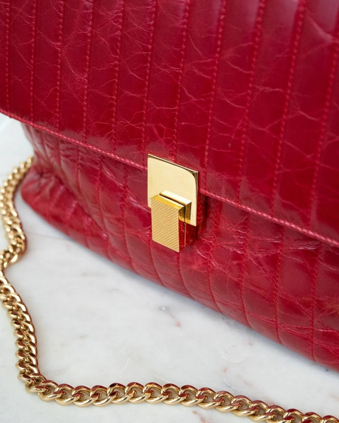 Red textured handbag with a gold chain strap on a marble surface