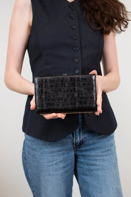 Person holding a black clutch bag against a neutral background