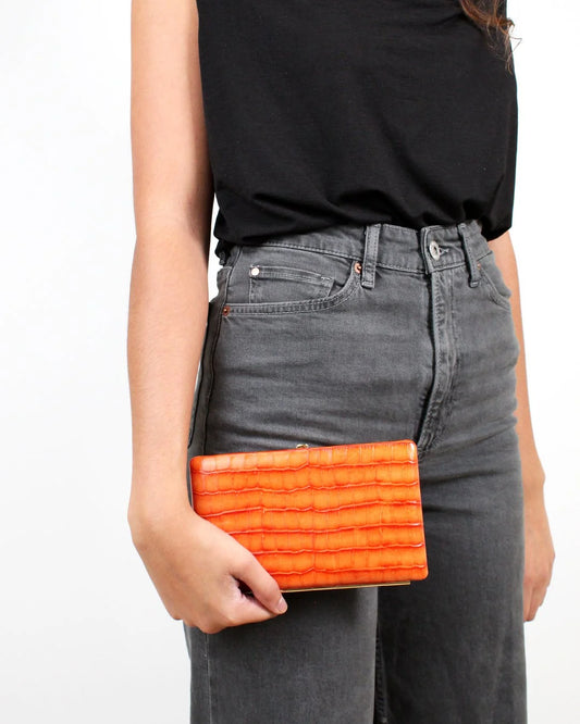 Person holding an orange clutch bag with a plain background