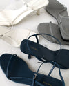 Navy, white, and gret sandals with 'The Row' branding on a light marble background