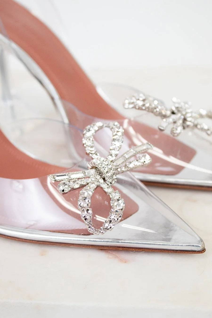 Clear high-heeled shoes with crystal bow design on a light background