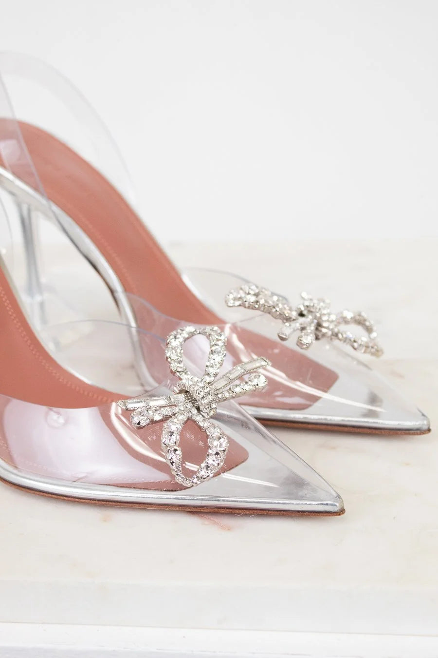 Clear high-heeled shoes with decorative bow and crystals on a light background