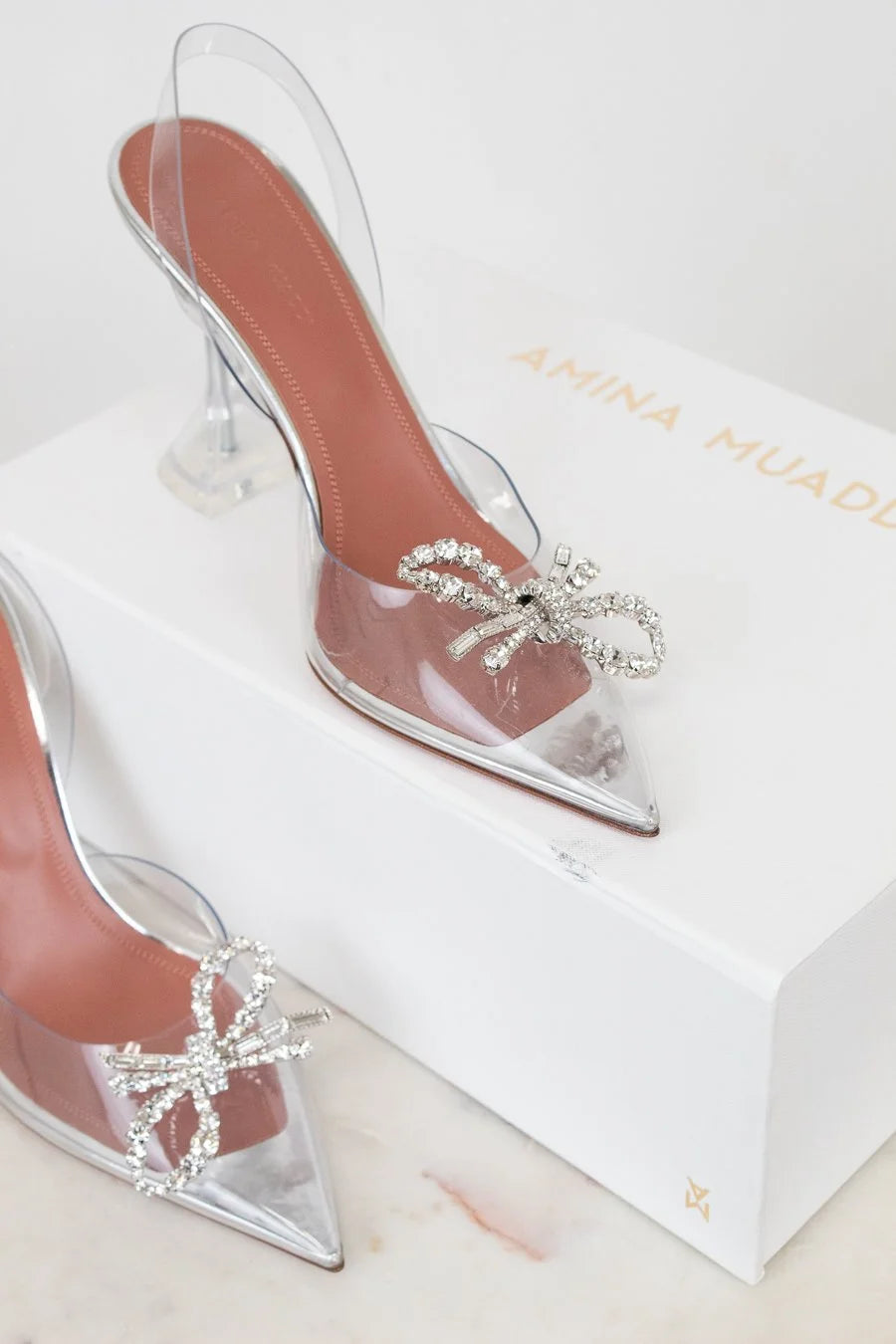 Clear high-heeled shoes with decorative bows on a branded box