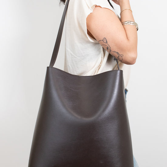 Person wearing a dark brown leather shoulder bag against a white background