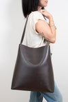 Person wearing a dark brown leather shoulder bag against a white background