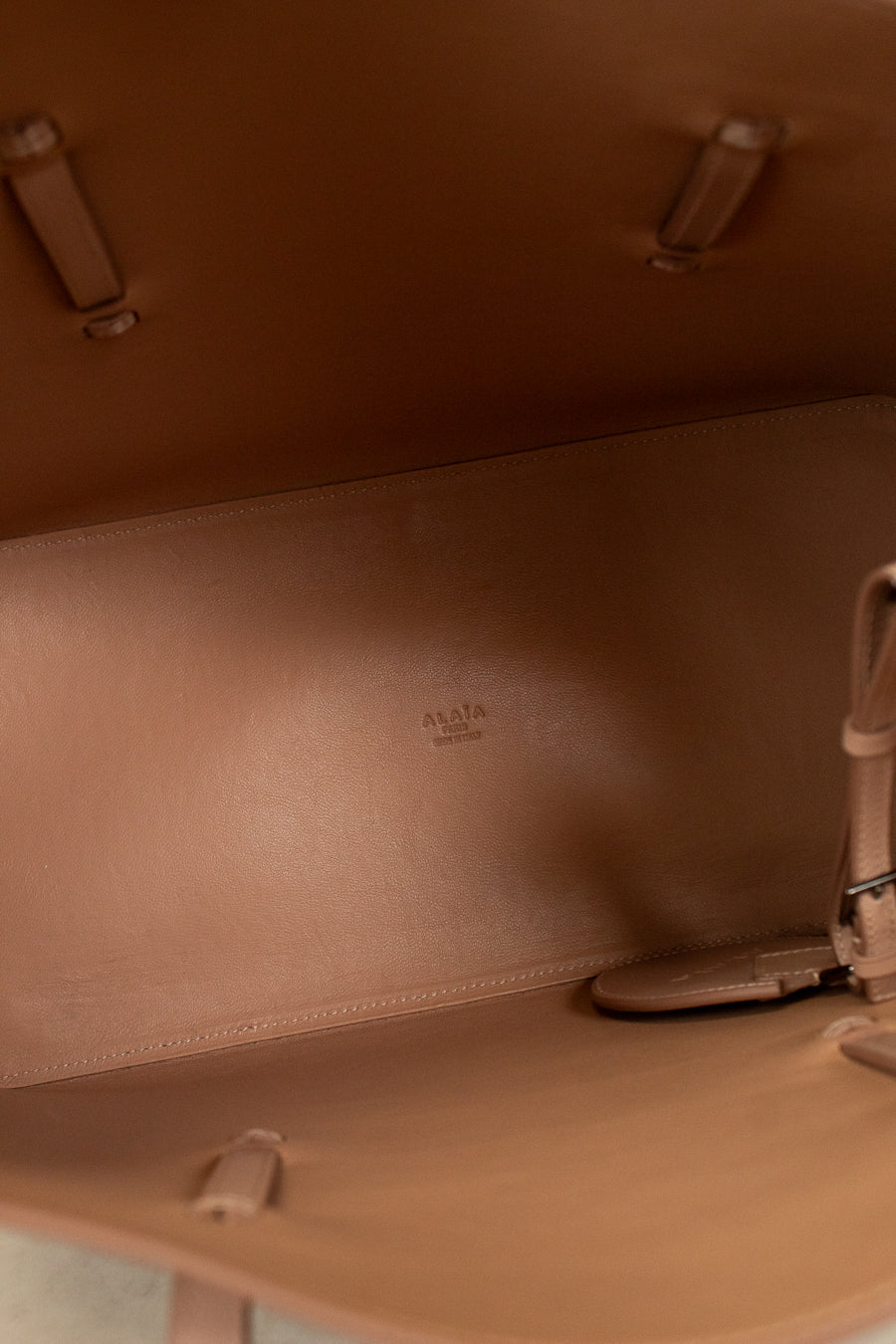 Close-up of a brown leather bag with visible stitching and a brand logo.