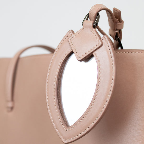 Close-up of a beige handbag with a small mirror attachment on a light gray background.