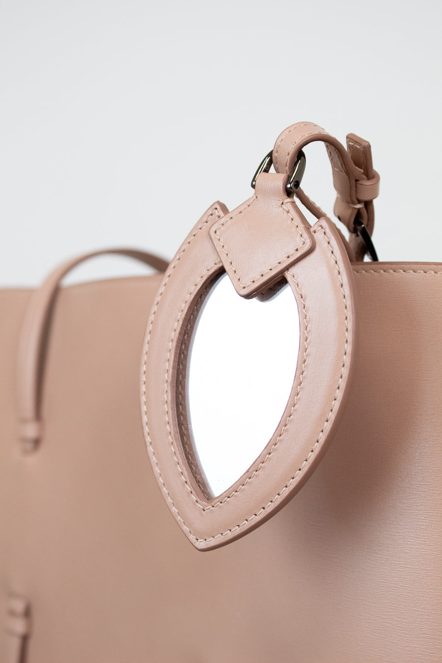 Close-up of a beige handbag with a small mirror attachment on a light gray background.