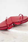 A red leather zippered handbag with thin straps and a silver zipper, resting on a white marble slab against a white background.