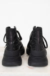 A pair of black chunky lace-up boots with glittery textured uppers, shown from the back on a light marble surface against a white background.
