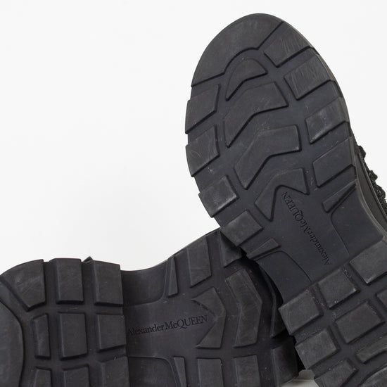Close-up of the treaded black rubber soles of a pair of boots, showing the lug pattern and embossed branding, set against a clean white background.