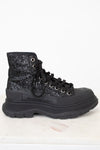 A black high-top lace-up boot with a glittery black and silver upper, black laces, and a chunky black sole, shown against a white background.