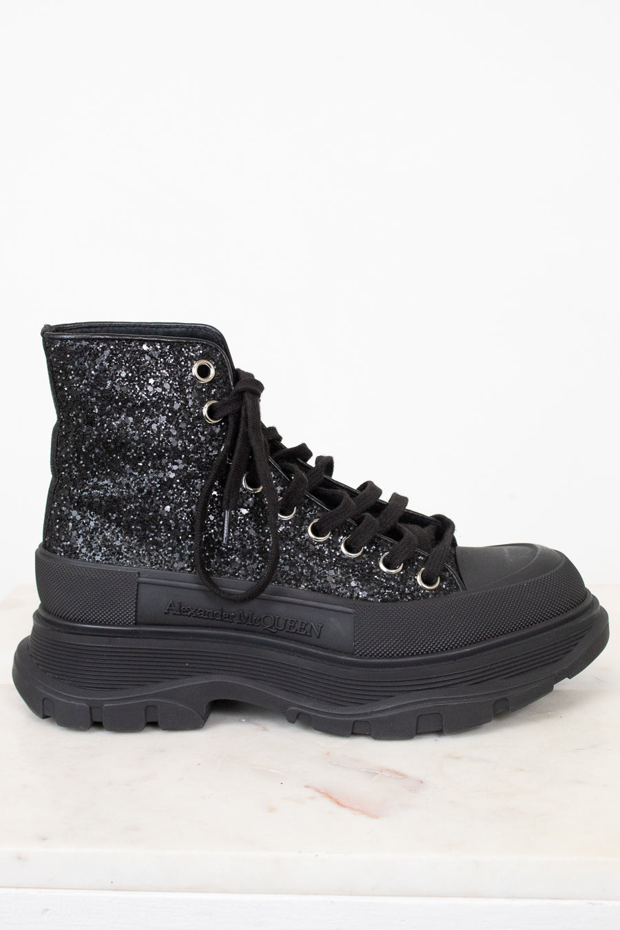 A black high-top lace-up boot with a glittery black and silver upper, black laces, and a chunky black sole, shown against a white background.