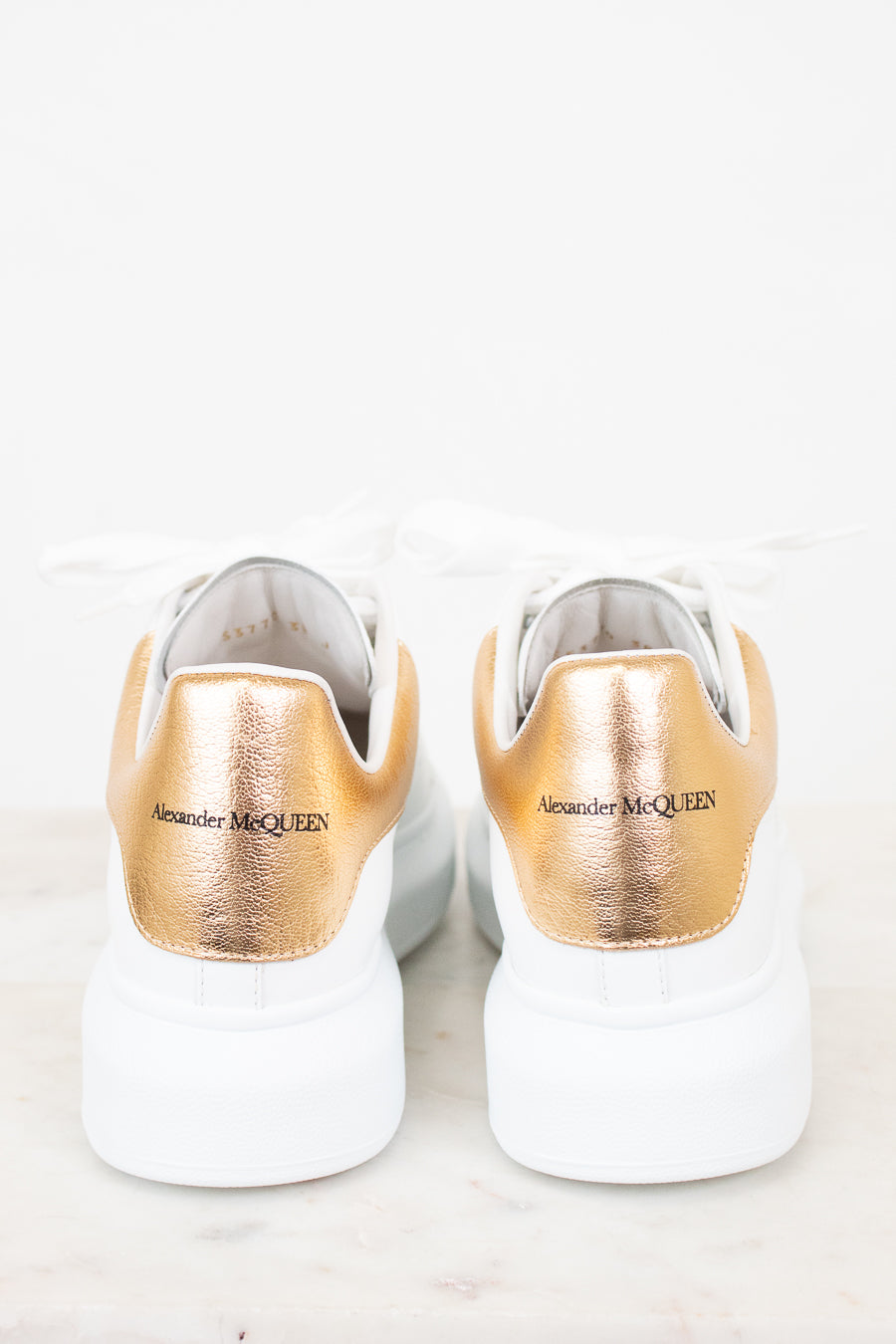 White sneakers with gold soles and 'Alexander McQueen' branding on a white background